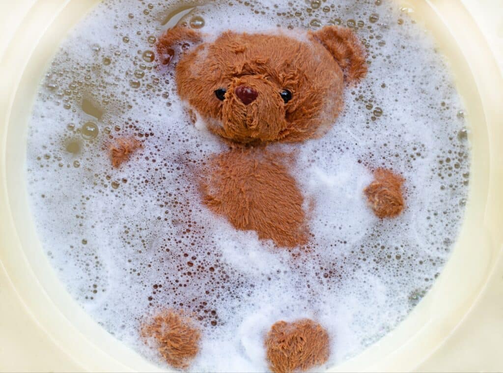 Hand washing a teddy bear toy in a basin of soapy water
