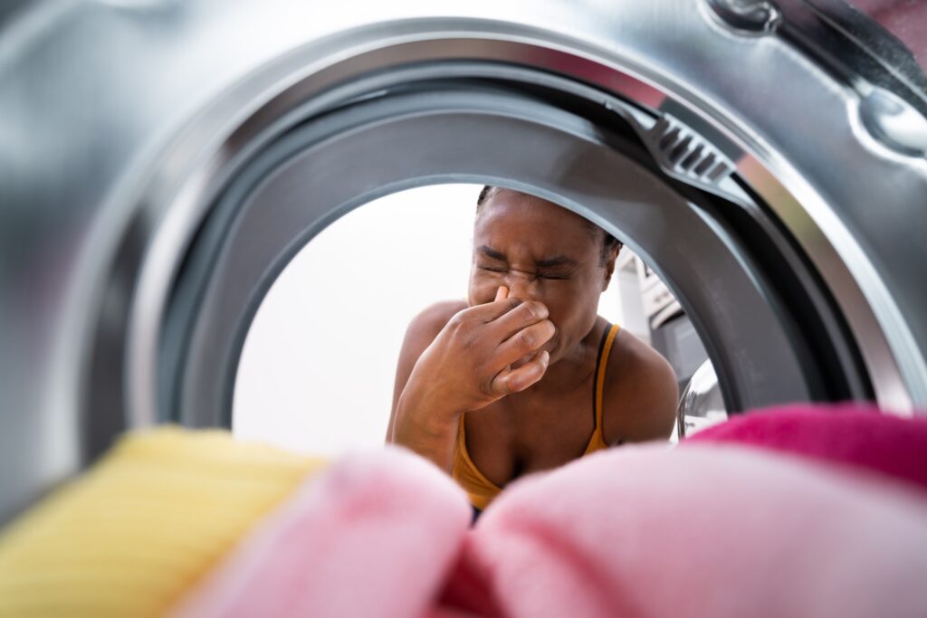 A person holding their nose in front of a washing machine, indicating a bad odor coming from the washer