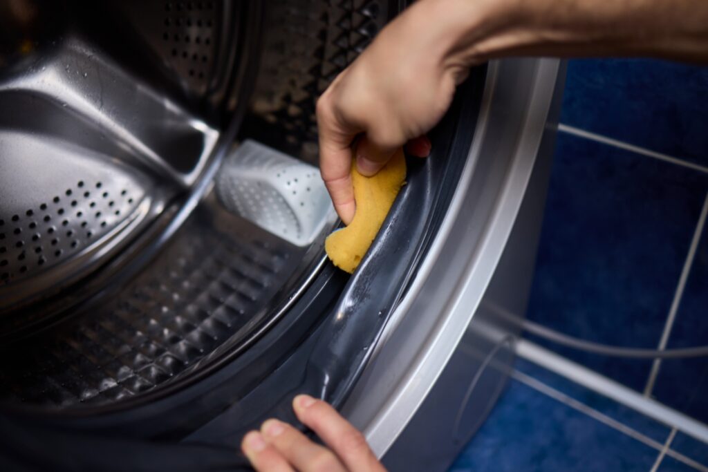 Cleaning a front-load washer - a hand in a rubber glove wiping around the rubber door gasket with a cloth