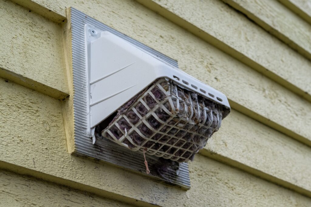 Exterior dryer vent cap on a house with lint buildup blocking the opening