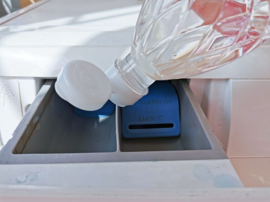 Vinegar being poured into a washing machine fabric softener compartment