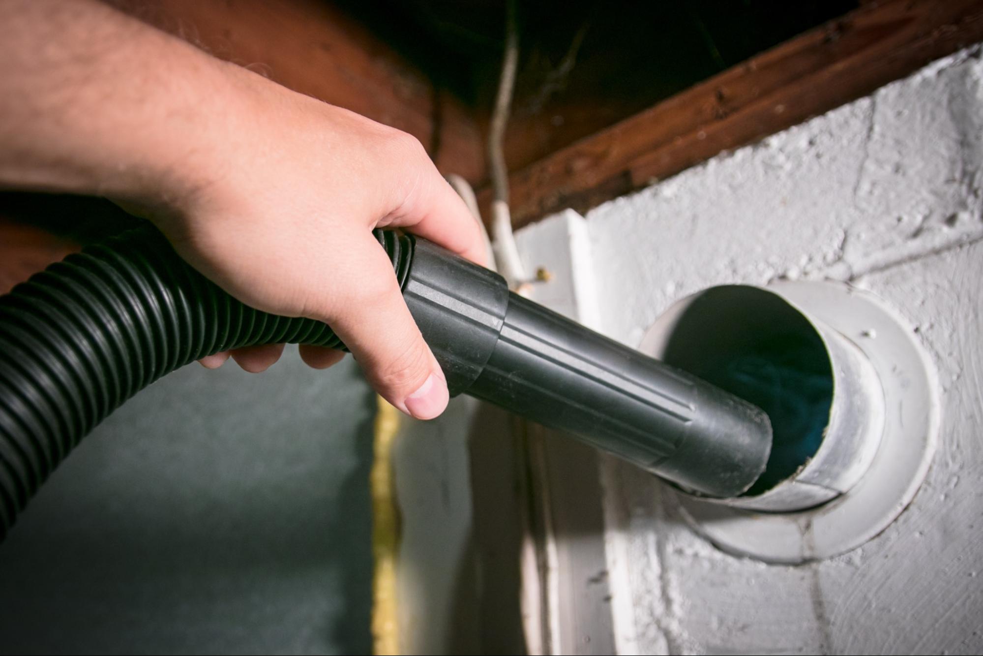 Hand inserting vacuum hose into wall vent