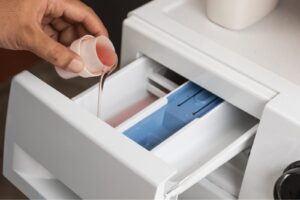 Person pouring measured liquid sport detergent into a washing machine dispenser